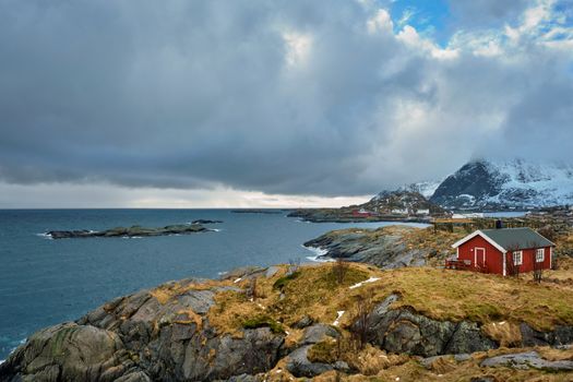 Clif with traditional red rorbu house on Litl-Toppoya islet on Lofoten Islands, Norway in winter