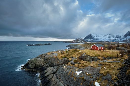 Clif with traditional red rorbu house on Litl-Toppoya islet on Lofoten Islands, Norway in winter
