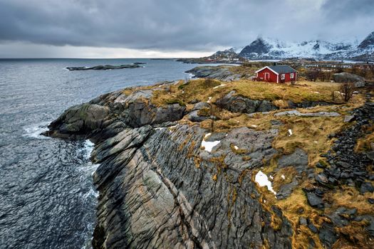 Clif with traditional red rorbu house on Litl-Toppoya islet on Lofoten Islands, Norway in winter