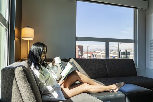 A gorgeous brunette model poses in lingerie as she reads a book in a home environment