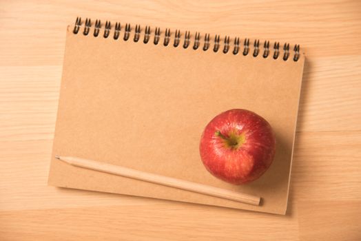 red apple on notebook with a pencil.