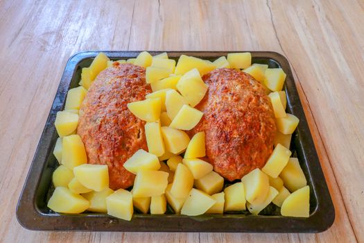 Baked minced pork and potatoes on a black baking pan. Homemade meat cutlets with potatoes in a cast iron pan served on a wooden table. Tasty and delicious lunch or dinner. Minced meat meatloaf baked.