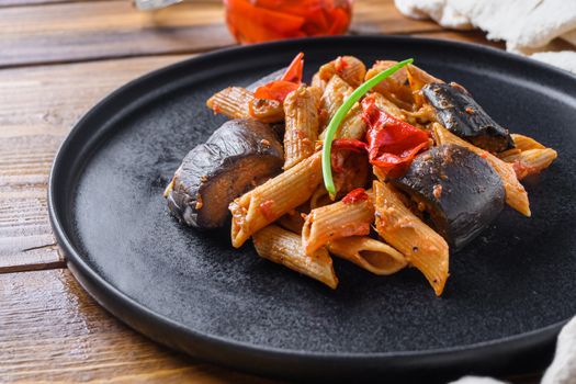 Aubergine penne eggplant pasta, pepper tomatoe sauce, on black plate over wooden table served side view