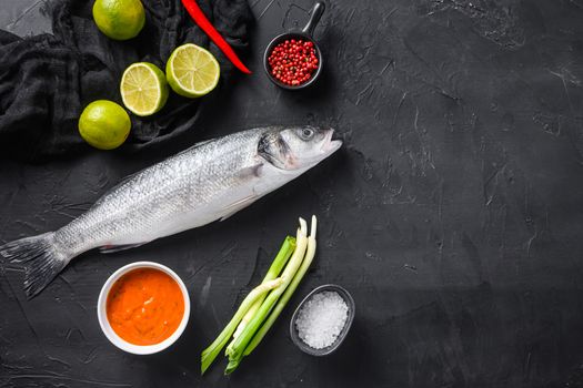 Raw seabass with spices and herbs ingredients on black background top view space for text