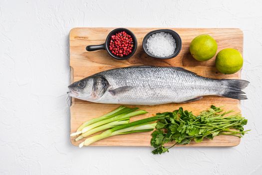 Whole sea bass with spices and herbs ingredients on chopping board over white textured background top view space for text