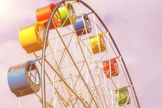 Ferris wheel with multi-colored cabs against the sky with clouds in the park on a sunny spring day.