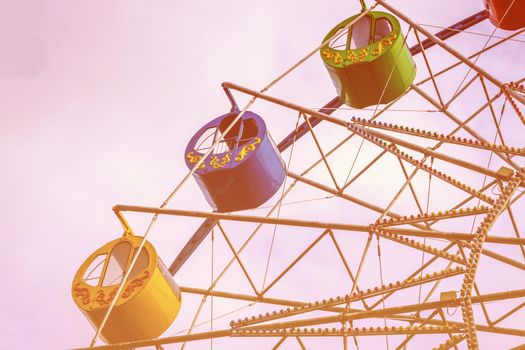 Ferris wheel with colorful cabs against the sky with clouds in the park on a sunny spring day.