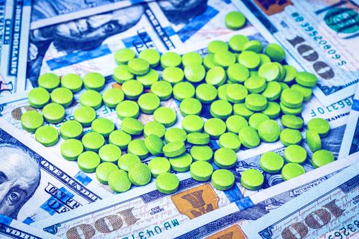 Green pills on the background of one hundred dollar bills. The concept of the expensive cost of healthcare or financing medicine.