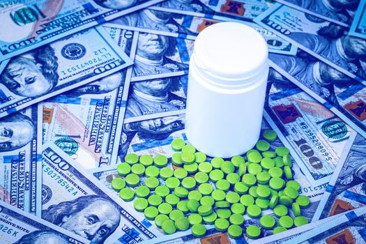 Green pills on the background of one hundred dollar bills. The concept of the expensive cost of healthcare or financing medicine. White medicine bottle with copy space for text.