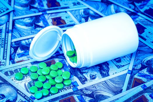 Green pills on the background of one hundred dollar bills. The concept of the expensive cost of healthcare or financing medicine. White medicine bottle with copy space for text.