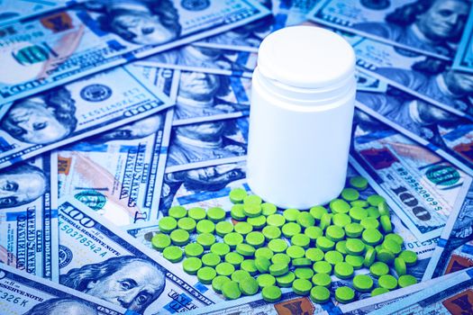 Green pills on the background of one hundred dollar bills. The concept of the expensive cost of healthcare or financing medicine. White medicine bottle with copy space for text.