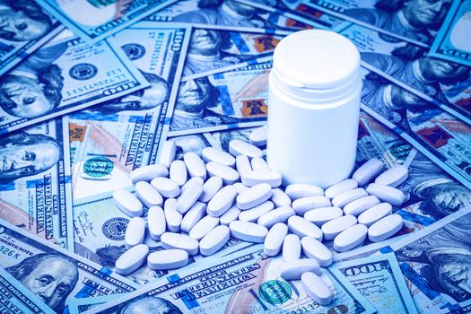 Pills on the background of hundred-dollar bills. The concept of the expensive cost of healthcare or financing medicine. White medicine bottle with copy space for text.