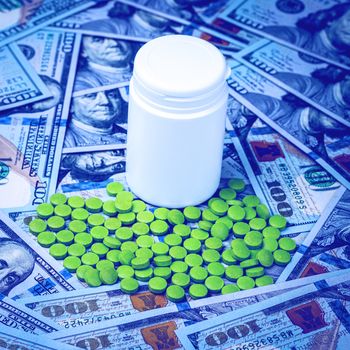 Green pills on the background of one hundred dollar bills. The concept of the expensive cost of healthcare or financing medicine. White medicine bottle with copy space for text.