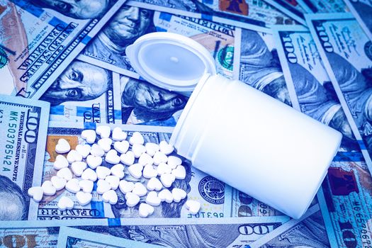 Heart-shaped pills on the background of hundred-dollar bills. The concept of the expensive cost of healthcare or financing medicine. White medicine bottle with copy space for text.