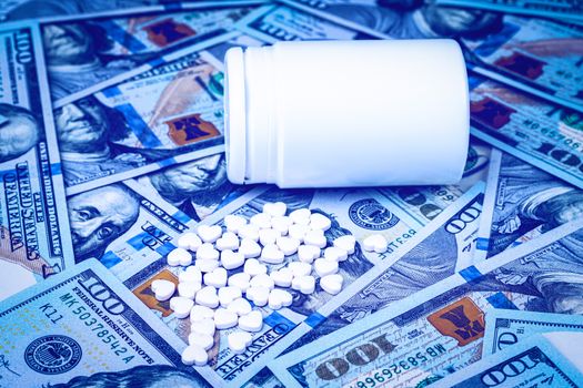 Heart-shaped pills on the background of hundred-dollar bills. The concept of the expensive cost of healthcare or financing medicine. White medicine bottle with copy space for text.