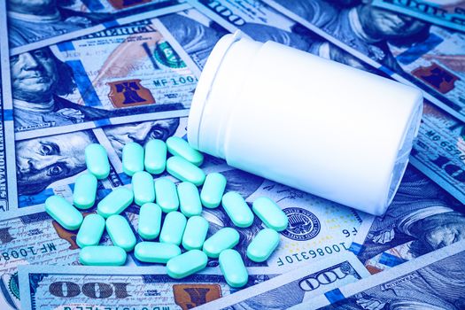 Green pills on the background of one hundred dollar bills. The concept of the expensive cost of healthcare or financing medicine. White medicine bottle with copy space for text.