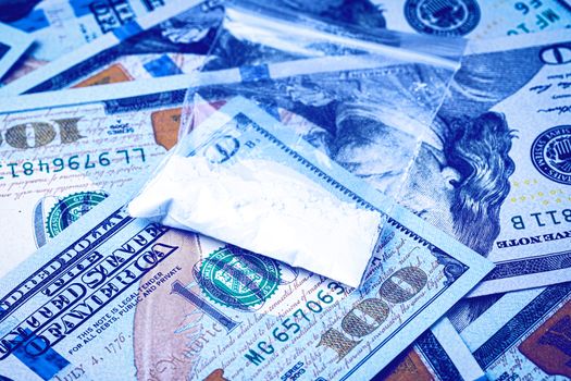 A bag with white narcotic powder like heroin or cocaine on the background of one hundred dollar bills. The concept of the use and sale of drugs.