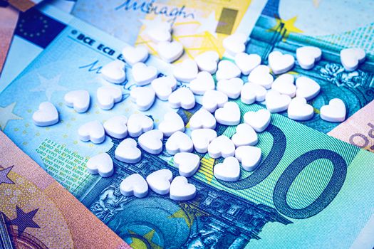 Heart-shape pills on the background of euro bills. The concept of the expensive cost of healthcare or financing medicine.