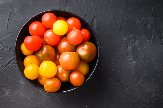 Cherry tomatoes in black bowl top view on black background space for text