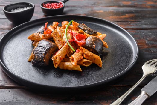 Aubergine penne eggplant pasta, pepper tomatoe sauce, on black plate over old dark wooden table served side view