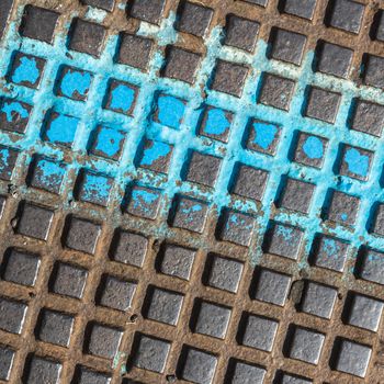 Close - up of a brown and blue manhole cover. Grunge metal background .