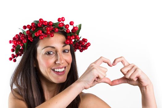 Christmas or New Year beauty woman portrait isolated on white background. Smiling young woman with wearing a Christmas wreath on her head making a heart with her hands. Natural makeup.
