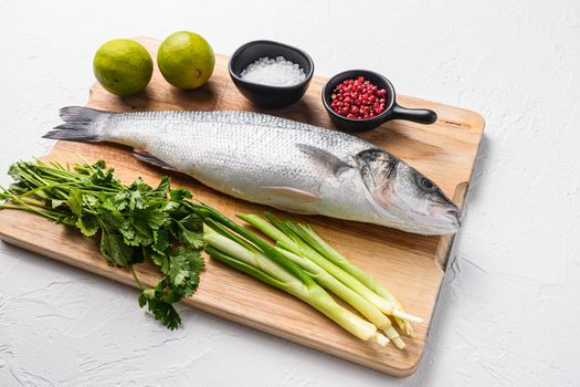 Whole sea bass with spices and herbs ingredients on chopping board over white textured background side view space for price.