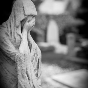 Old statue of a woman crying into her hands. Defocused blurry background.