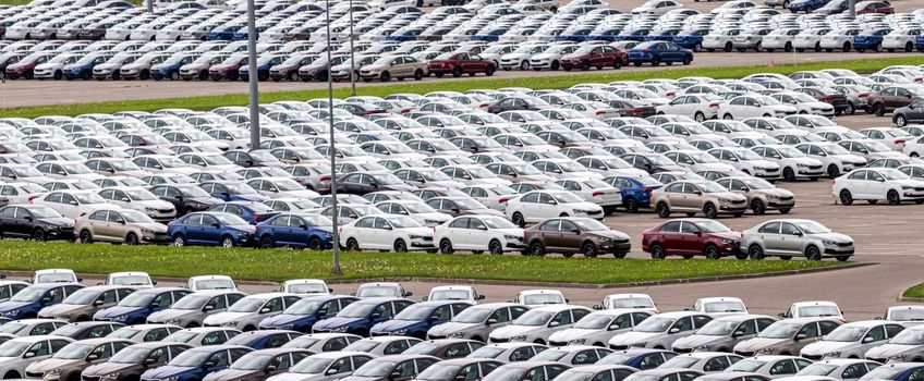 Rows of a new cars parked in a distribution center on a cloudy day in the spring, a car factory. Top view to the parking in the open air.