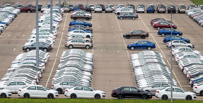 Rows of a new cars parked in a distribution center on a cloudy day in the spring, a car factory. Top view to the parking in the open air.