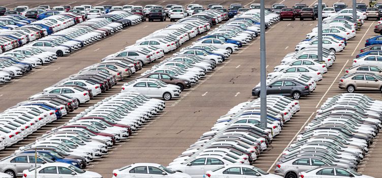 Rows of a new cars parked in a distribution center on a car factory on a cloudy day. Top view to the parking in the open air.