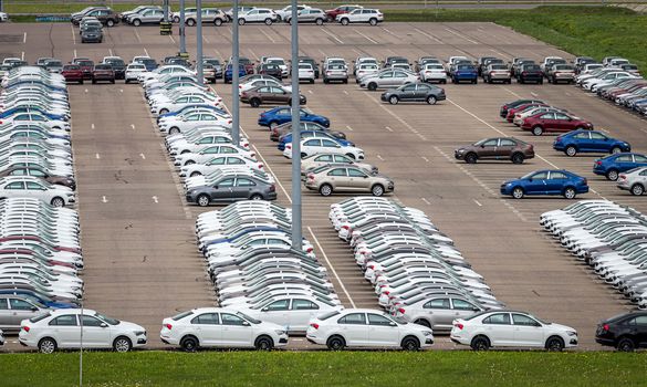 Rows of a new cars parked in a distribution center on a car factory on a cloudy day. Top view to the parking in the open air.