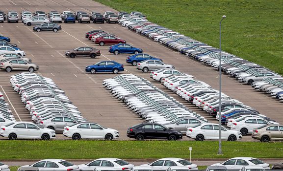 Rows of a new cars parked in a distribution center on a cloudy day in the spring, a car factory. Top view to the parking in the open air.