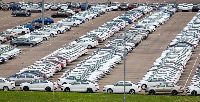 Rows of a new cars parked in a distribution center on a cloudy day in the spring, a car factory. Top view to the parking in the open air.