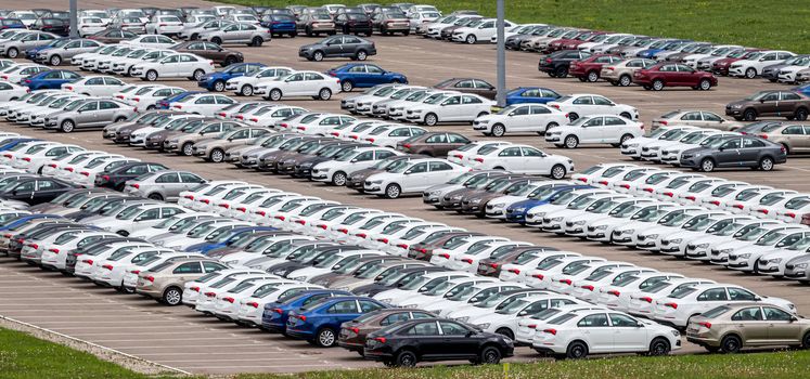 Rows of a new cars parked in a distribution center on a cloudy day in the spring, a car factory. Top view to the parking in the open air.