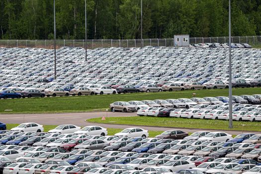 Rows of a new cars parked in a distribution center of a car factory. Top view to the parking in the open air.