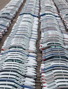 Rows of a new cars parked in a distribution center on a cloudy day in the spring, a car factory. Top view to the parking in the open air.