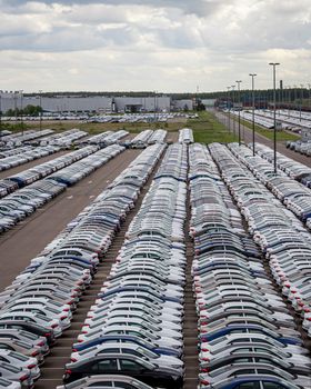 Rows of a new cars parked in a distribution center on a cloudy day in the spring, a car factory. Top view to the parking in the open air.