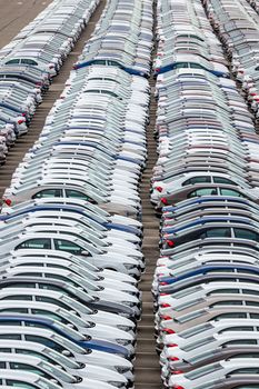 Rows of a new cars parked in a distribution center on a car factory on a cloudy day. Top view to the parking in the open air.