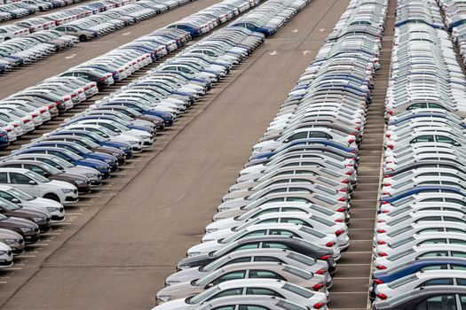 Rows of a new cars parked in a distribution center on a cloudy day in the spring, a car factory. Top view to the parking in the open air.