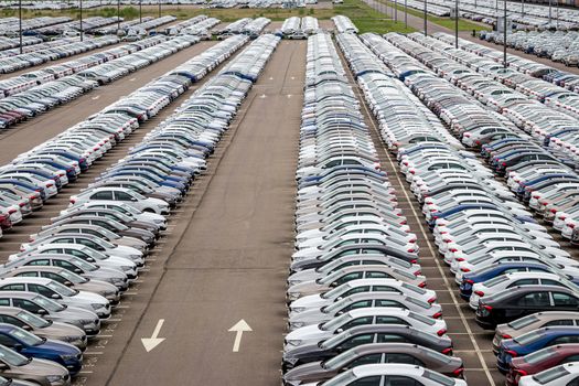 Rows of a new cars parked in a distribution center of a car factory. Top view to the parking in the open air.