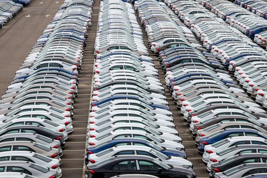 Rows of a new cars parked in a distribution center of a car factory. Top view to the parking in the open air.