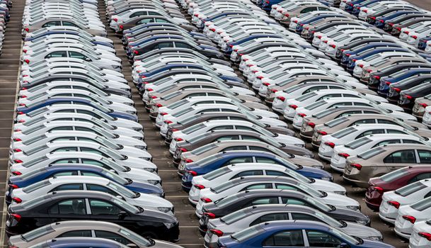 Rows of a new cars parked in a distribution center on a car factory on a cloudy day. Top view to the parking in the open air.