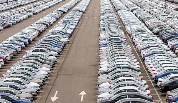 Rows of a new cars parked in a distribution center of a car factory. Top view to the parking in the open air.