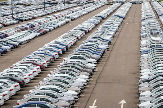 Rows of a new cars parked in a distribution center on a car factory on a cloudy day. Top view to the parking in the open air.