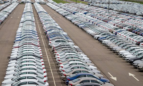 Rows of a new cars parked in a distribution center of a car factory. Top view to the parking in the open air.