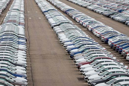 Rows of a new cars parked in a distribution center on a cloudy day in the spring, a car factory. Top view to the parking in the open air.