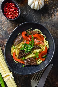 Chinese noodles with vegetables and beef in black bowl top view close up.