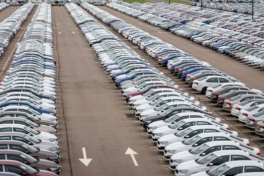 Rows of a new cars parked in a distribution center on a cloudy day in the spring, a car factory. Top view to the parking in the open air.