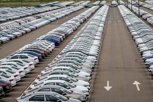 Rows of a new cars parked in a distribution center of a car factory. Top view to the parking in the open air.